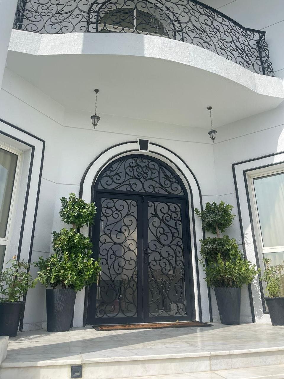 Arched entrance with ornate wrought-iron double doors flanked by potted plants.