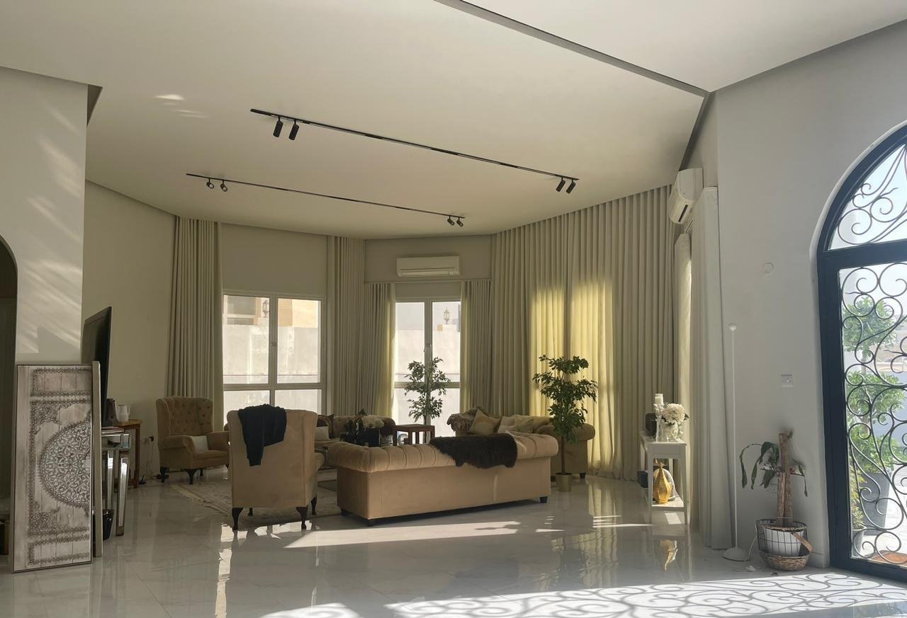 Sunlit salon with an arched iron-latticed window casting patterned shadow across a marble floor.