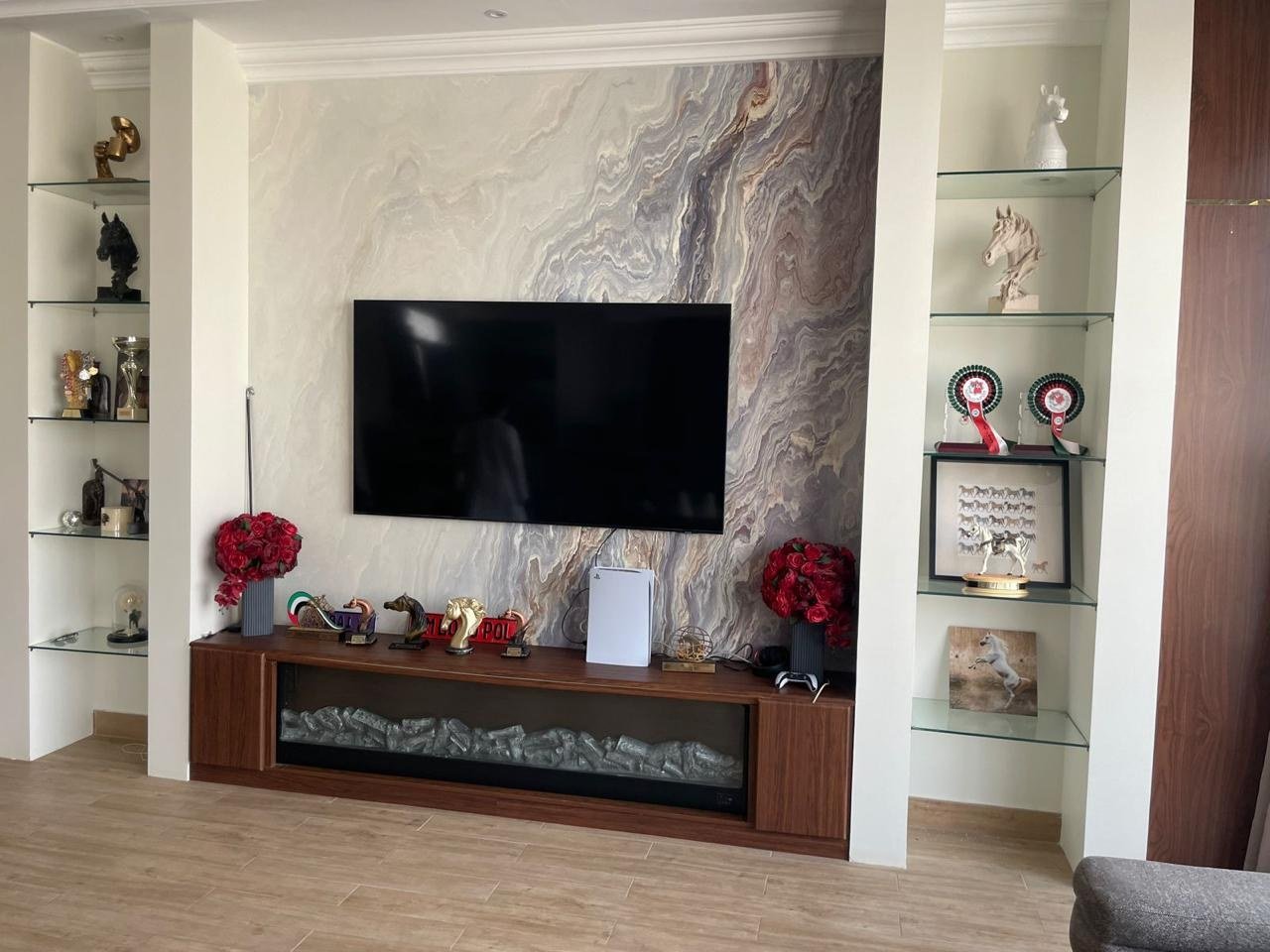 Book-matched marble feature wall with a linear fireplace and equestrian trophies on glass shelves.