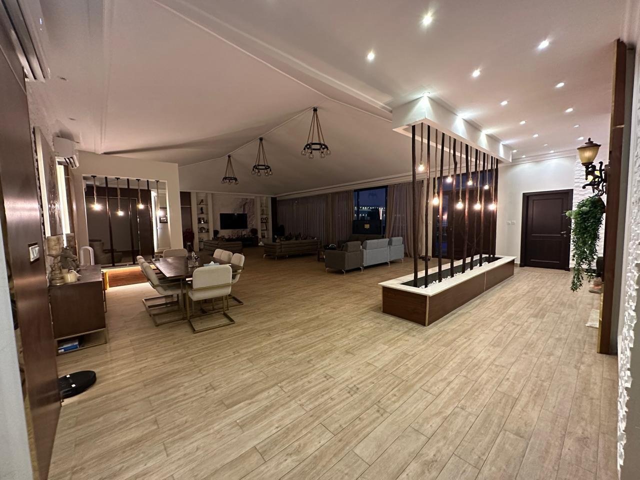 Majlis seating running the length of a timber-floored hall behind a planted divider.