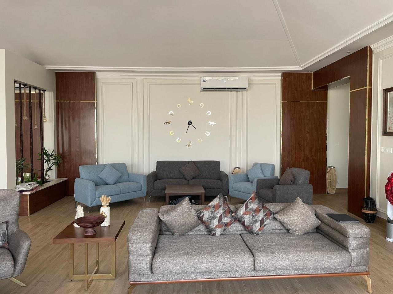 Formal salon with pale blue armchairs, a long sofa and a sunburst wall clock.