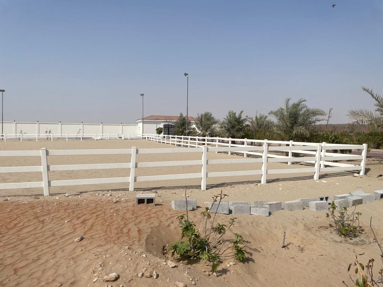 White post-and-rail ranch fencing running across bare sand under a clear sky.