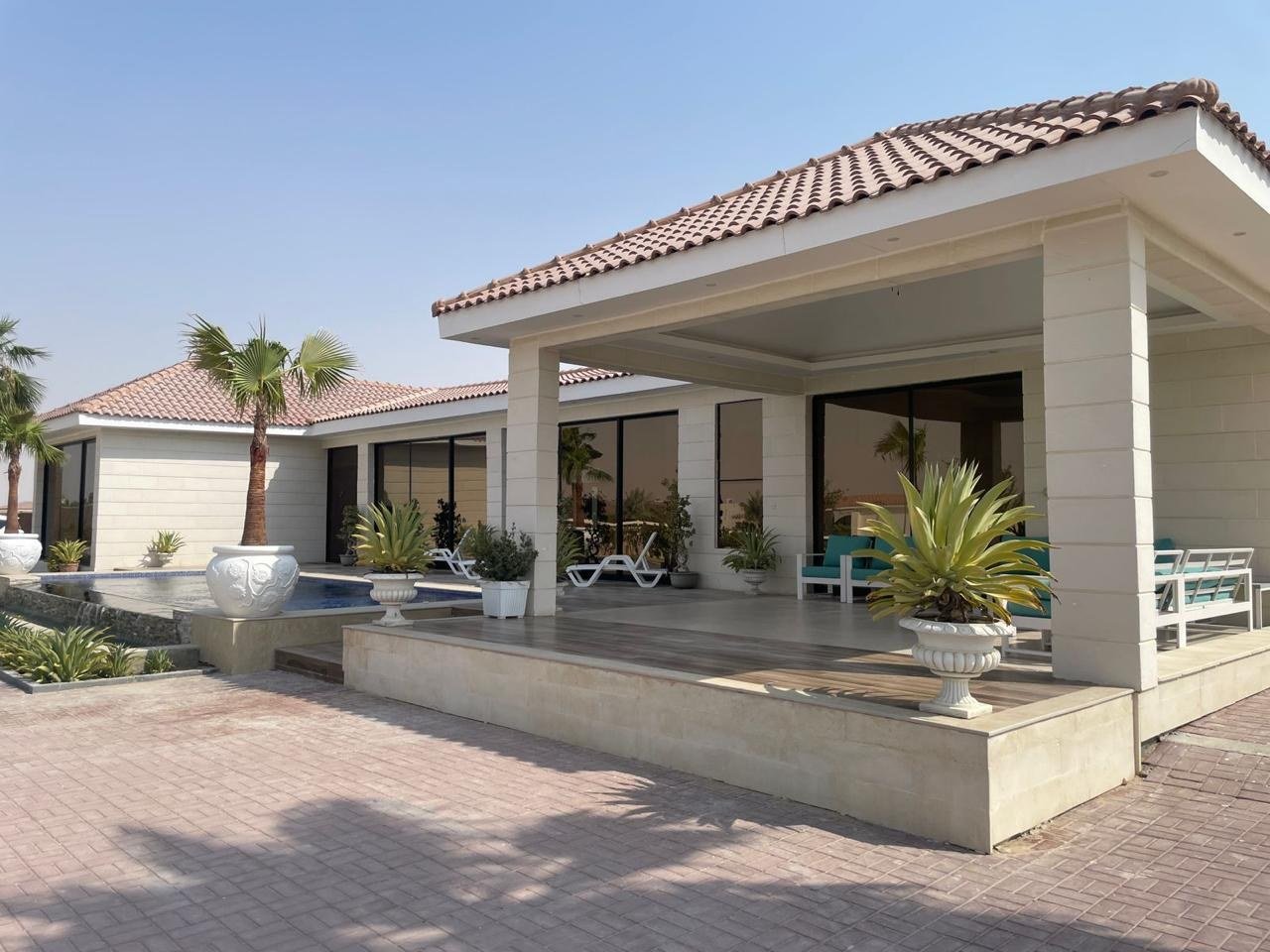 Paved approach leading to the pavilion with tinted glazing reflecting the palms.