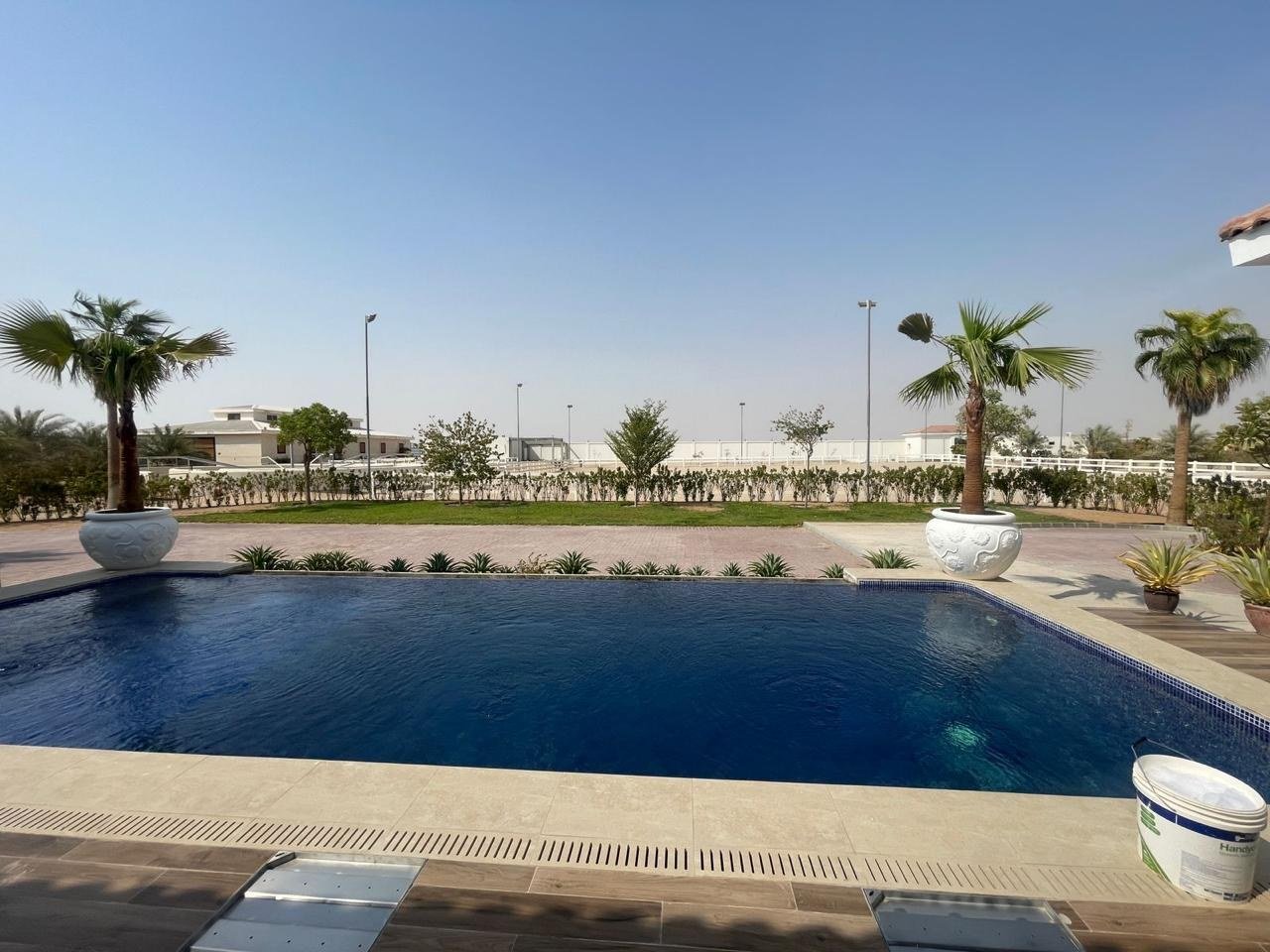 Wide view of the estate pool with palms and white perimeter fencing beyond.