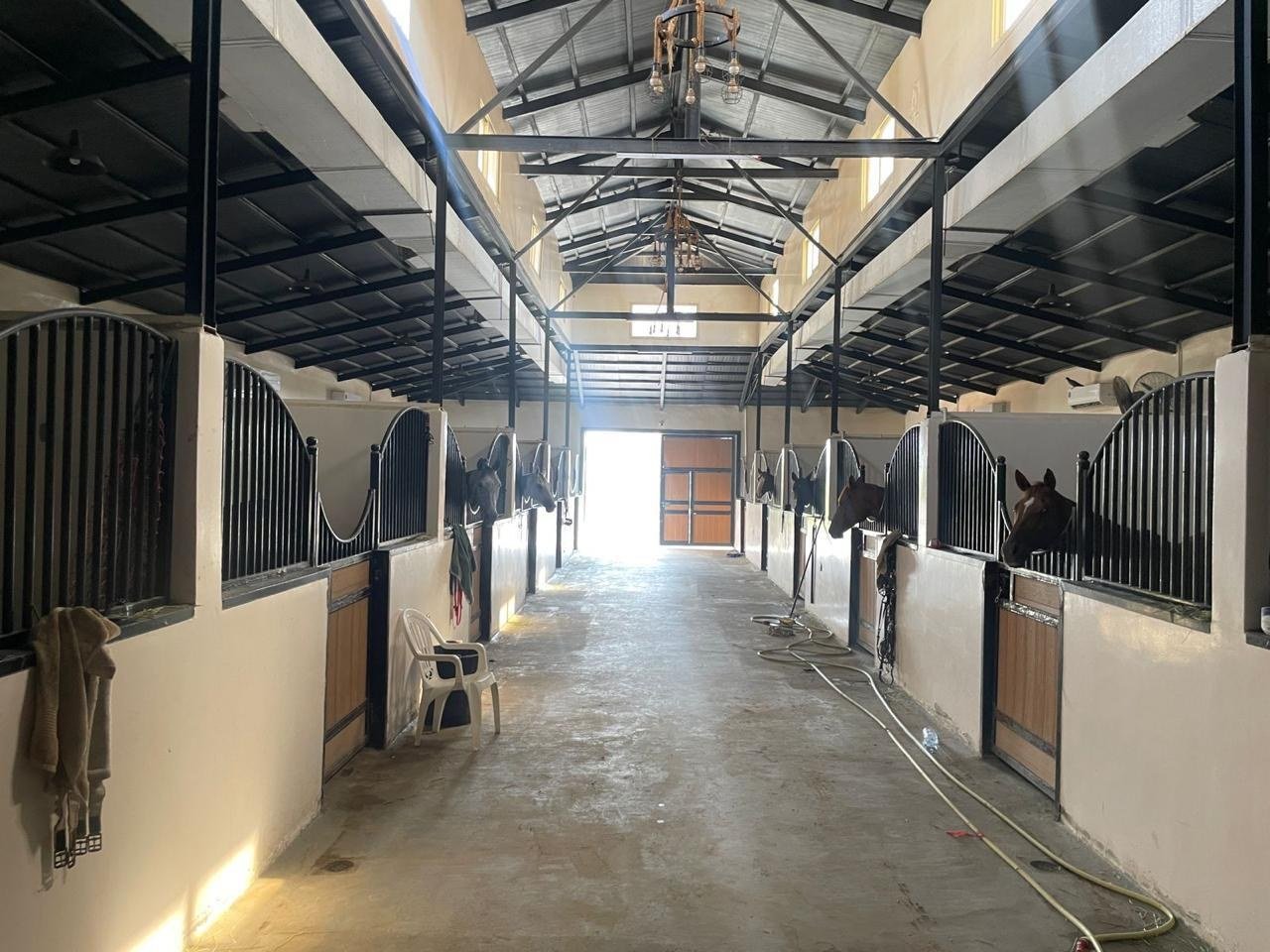 Wide concrete stable aisle running towards an open doorway blown out with daylight.