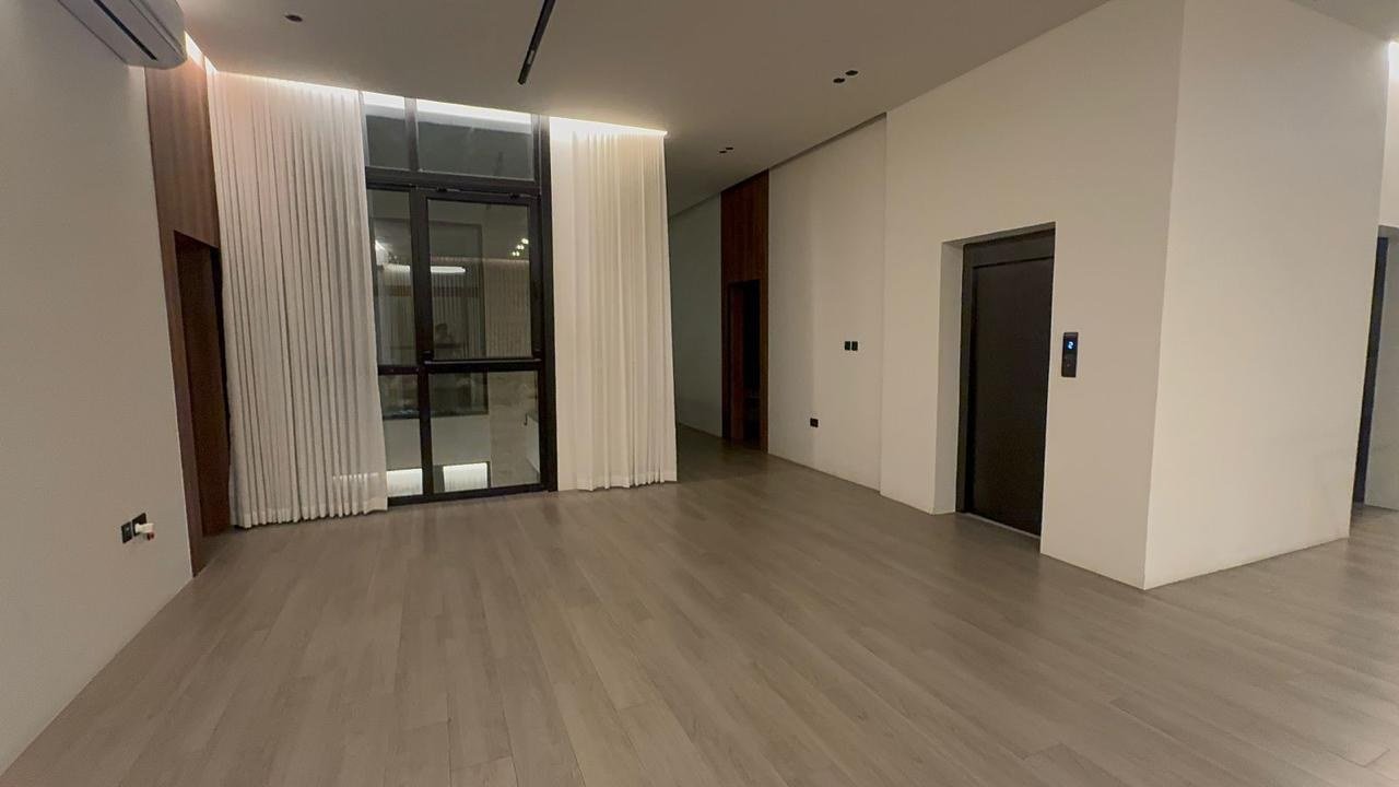 Empty room with full-height sliding glazing and sheer drapes over a timber floor.